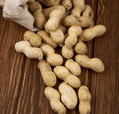 side view of peanuts in shell scattered from a sack on wooden background